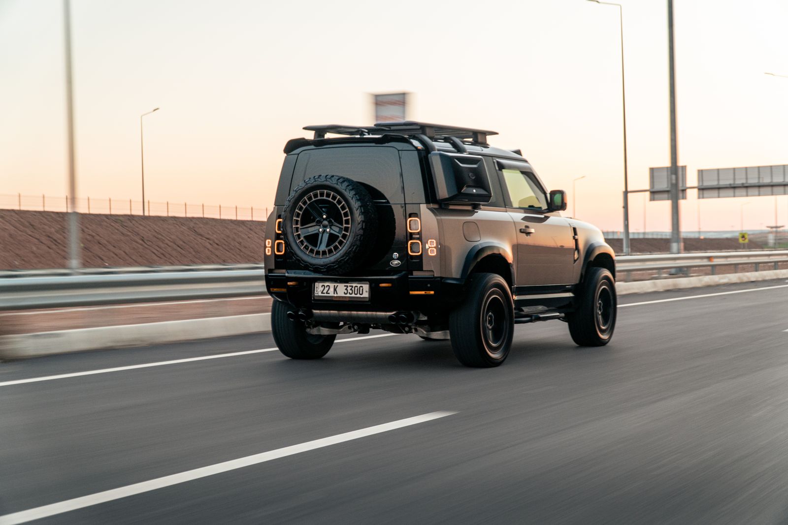 Black Land Rover Defender travelling on an open road at sunset